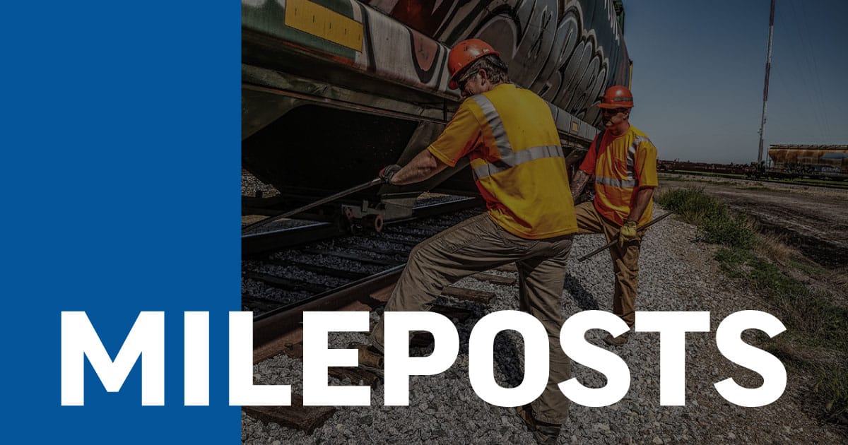 An image of two male Northern Plains Railroad employees performing maintenance on a locomotive in a rural area.