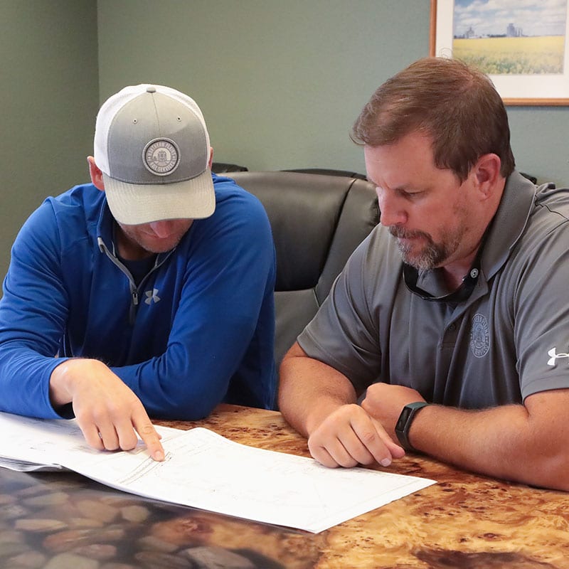 Two male Northern Plains Railroad employees going over a rail design on paper in a conference room.