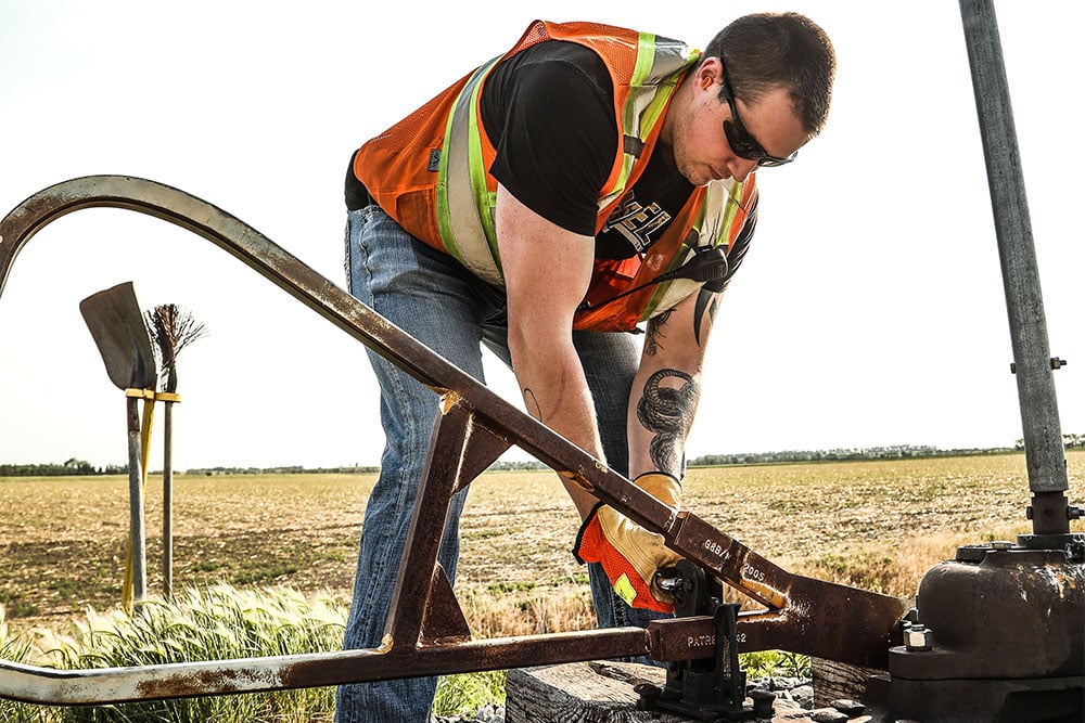 A male Northern Plains Railroad employee bending down to repair a train track switch.