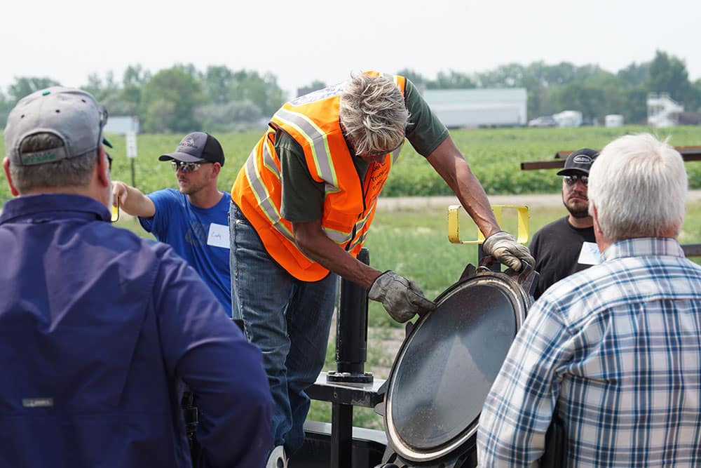 Man in an orange safety vest and heavy-duty work gloves instructs on tank car construction and operations.